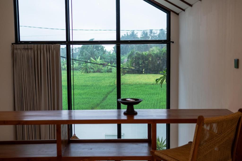 A tall gable window framing a bright green rice field, with a timber table in the foreground