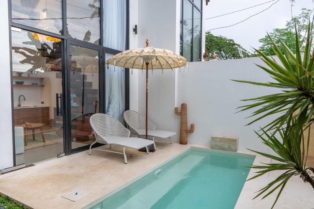 Private pool beside a villa terrace, with two loungers and a Balinese parasol, seen through open glass doors