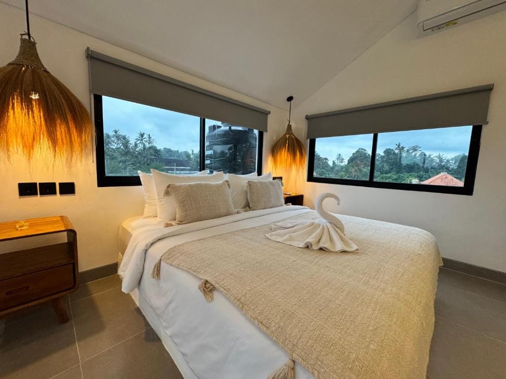 Bedroom under a pitched ceiling with rattan pendant lights and windows onto the treetops