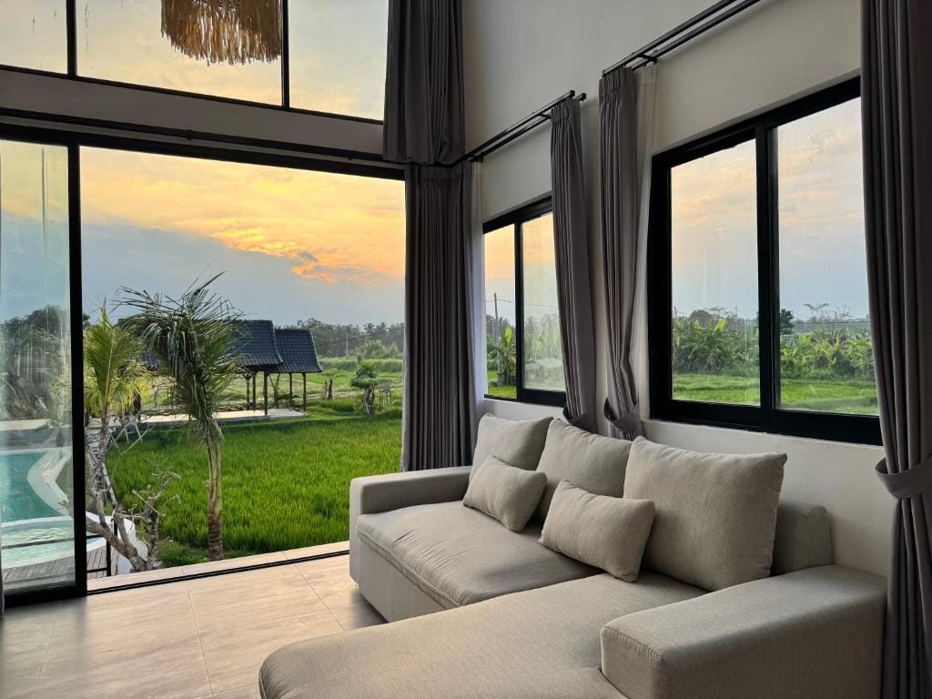 Villa living room at sunset, with full-height glass opening onto the pool and the rice field beyond